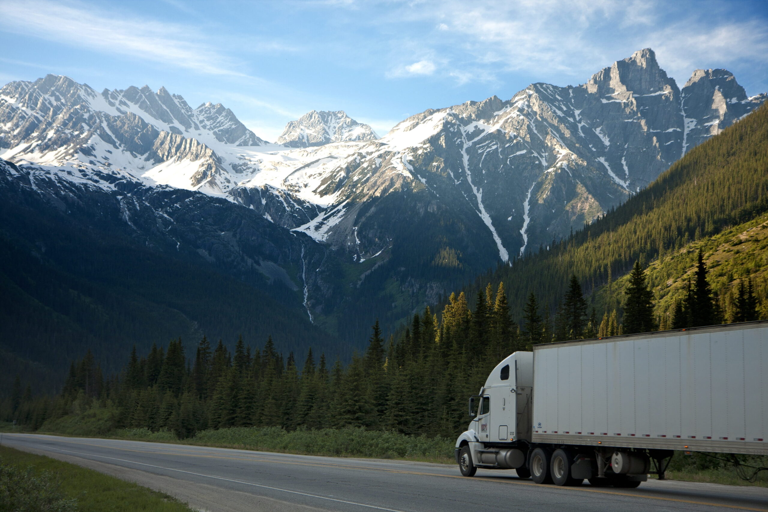 White semi truck driving down highway in front of rocky mountains