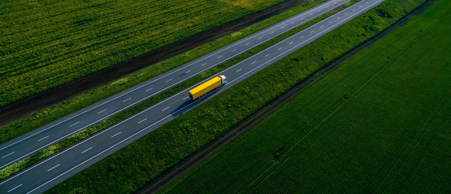 yellow truck driving on asphalt road along the green fields